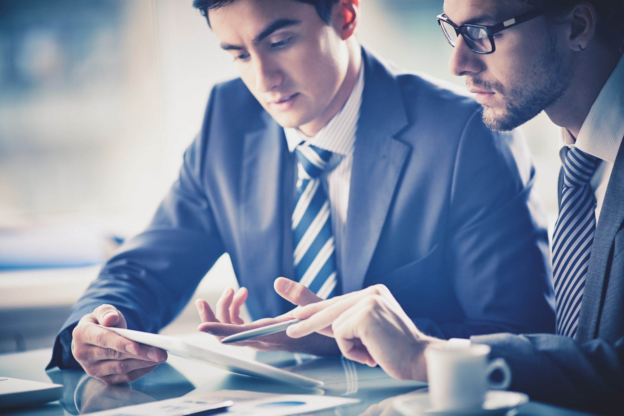 Image of two young businessmen discussing document in touchpad at meeting